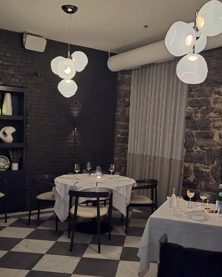 Mare dining room with exposed stone walls, a checkerboard floor, white-clothed tables and sculptural pendant lights.