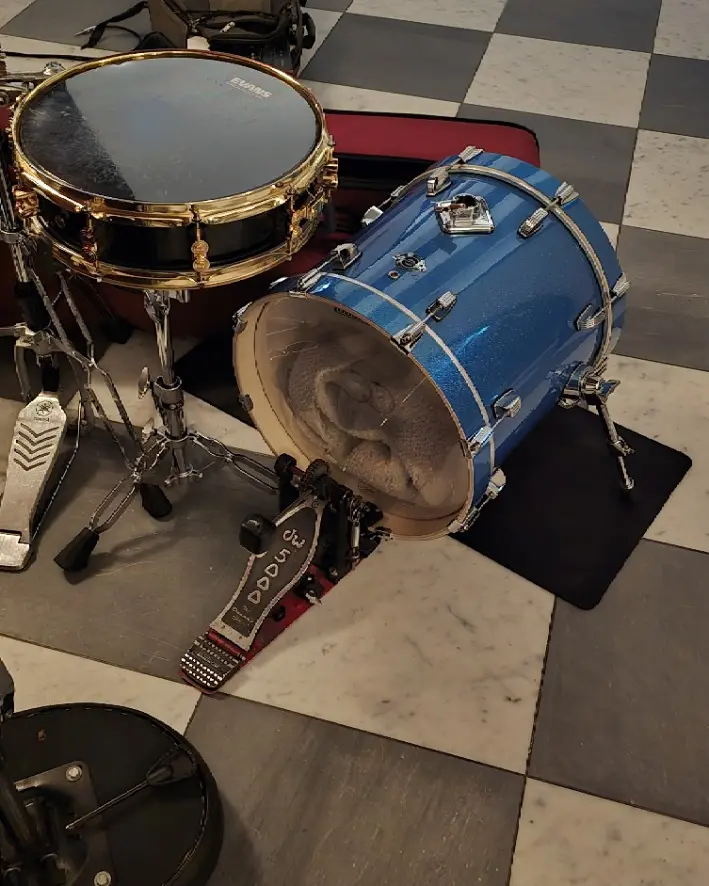 Compact blue kick drum and black-and-gold snare arranged on Mare’s checkerboard floor.