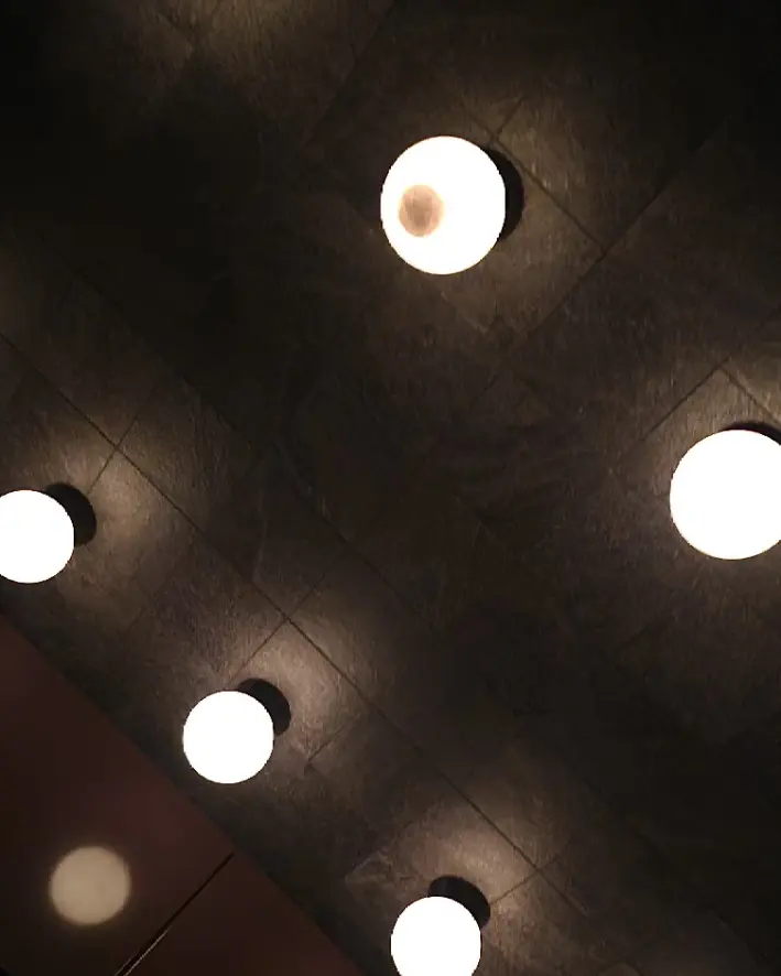 Round ceiling lights reflected across dark glossy surfaces inside Mare.